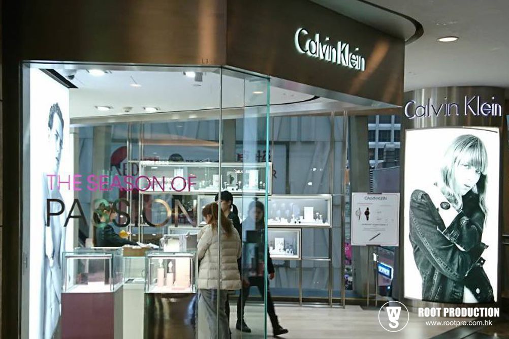 Calvin Klein store front in a mall, displaying watches and advertisements. Two people are entering.