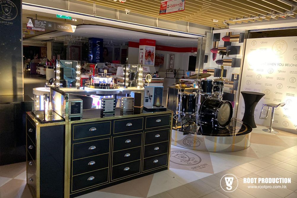 Cosmetics display in a mall. Black and gold counter with beauty products and mirrors. Drum set and sign in background.