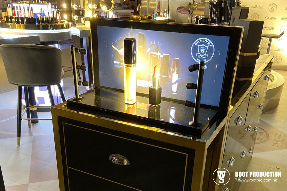 Makeup display with a lit-up screen, lipstick, and other products in a store. Black and gold tones.