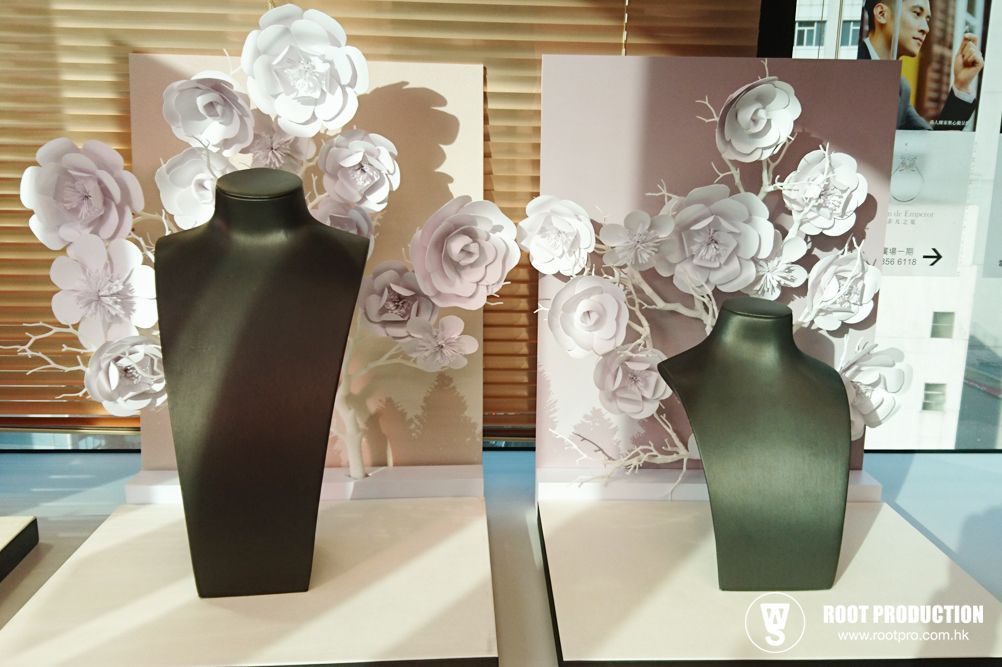 Two black necklace displays with paper flower decorations on a white table.
