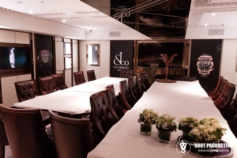 A luxury dining room with a long table set for a formal event. Dark decor, watch displays, and floral centerpieces.