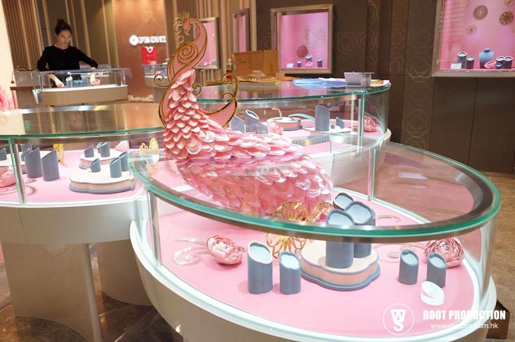 Jewelry store display with pink peacock, glass cases, and jewelry, with a person behind a counter.