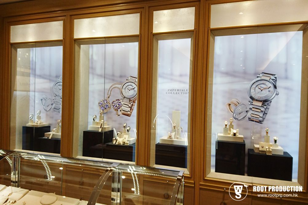 Jewelry store display windows with watches and jewelry on black platforms. Light wood trim, soft lighting.