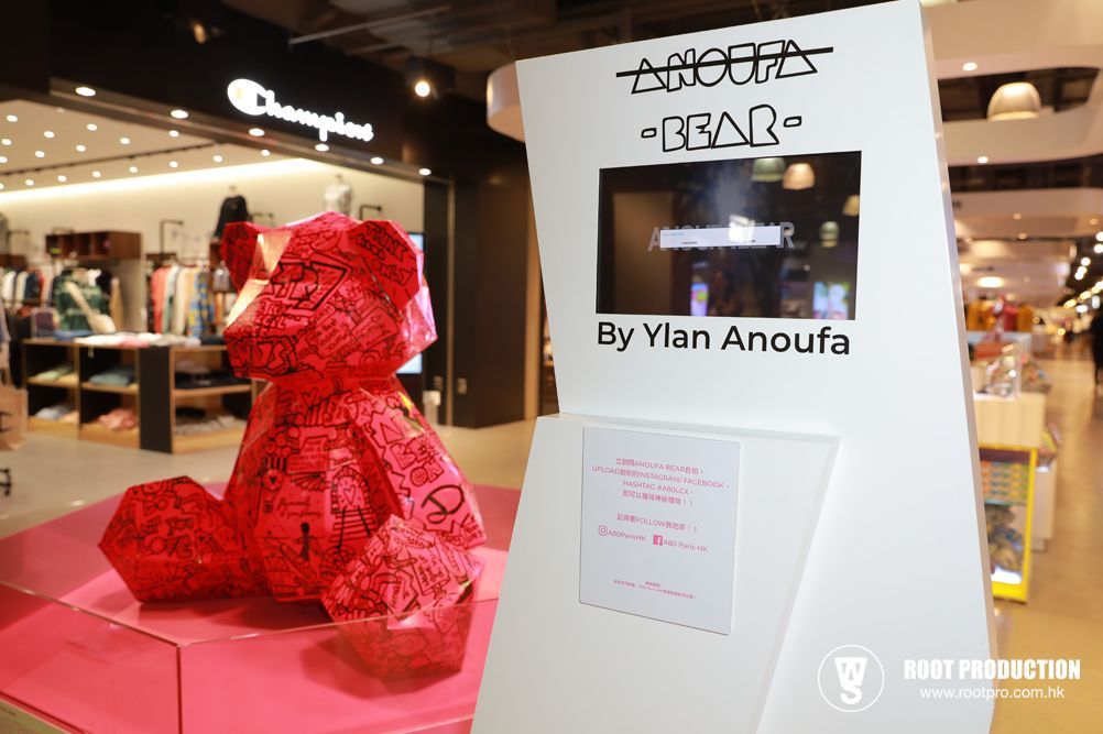 Red paper bear sculpture by Ylan Anoufa in a store. Champion shop in the background. Pink pedestal and display stand.