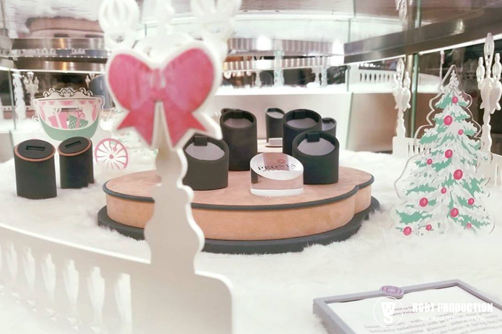 A Christmas window display with a bow, Christmas tree, and jewelry on a snowy platform.