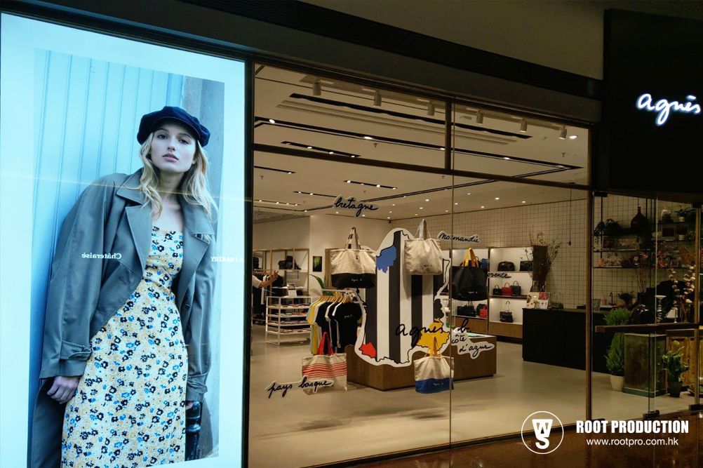 Woman in front of an Agnes B store, wearing a dress and a coat. The store's interior is visible.
