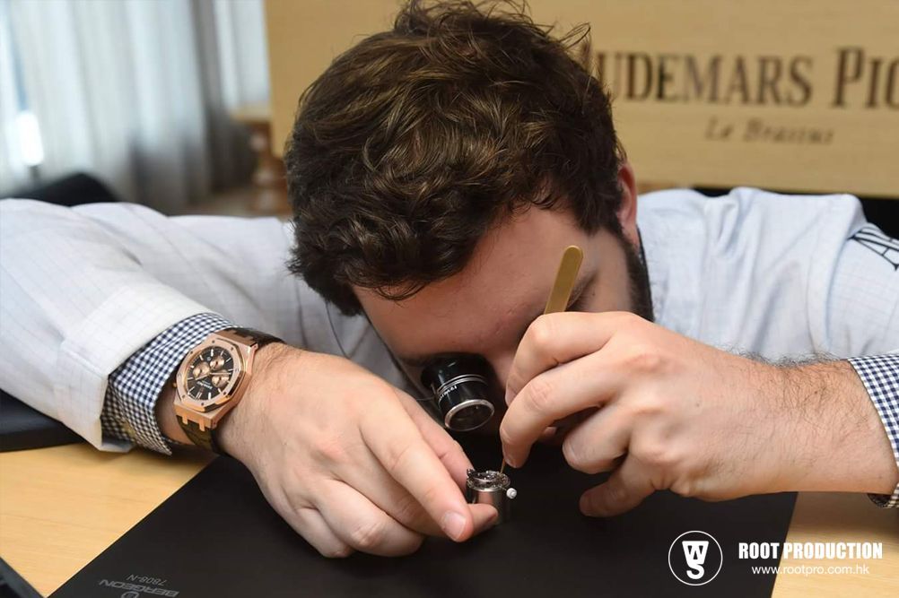 Man inspecting a watch with a loupe, wearing a gold watch. White lab coat, blurred background, close up.