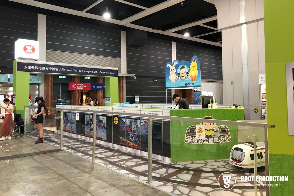 Inside a train station, people stand near displays and ticket windows; a model train is on display.