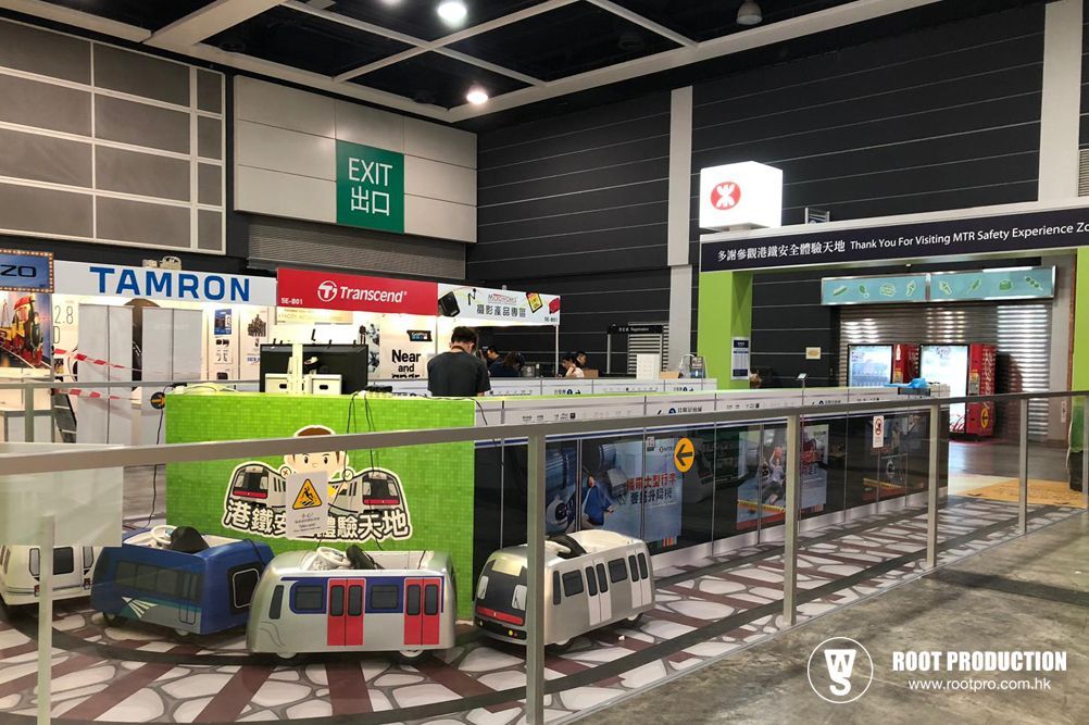 Exhibition hall with displays, people, and toy trains. Green, white, and black colors dominate the scene.