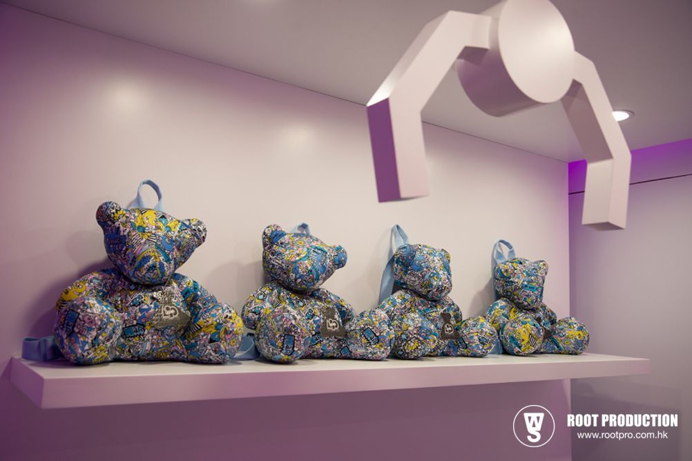 Four colorful teddy bear sculptures on a shelf, with a claw machine arm above them.