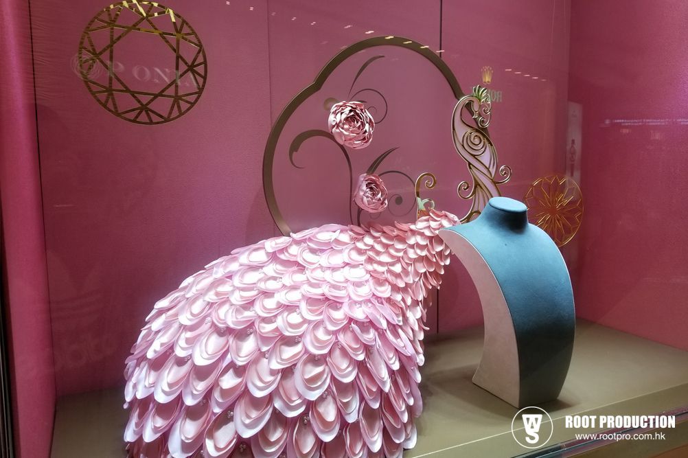 Pink jewelry display with peacock tail and blue necklace form.