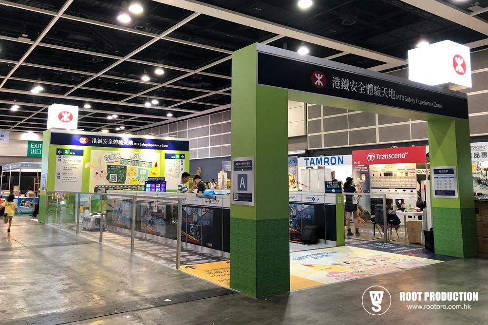 Entrance to a trade show booth with green pillars and a large overhead sign. People are walking around the booth.
