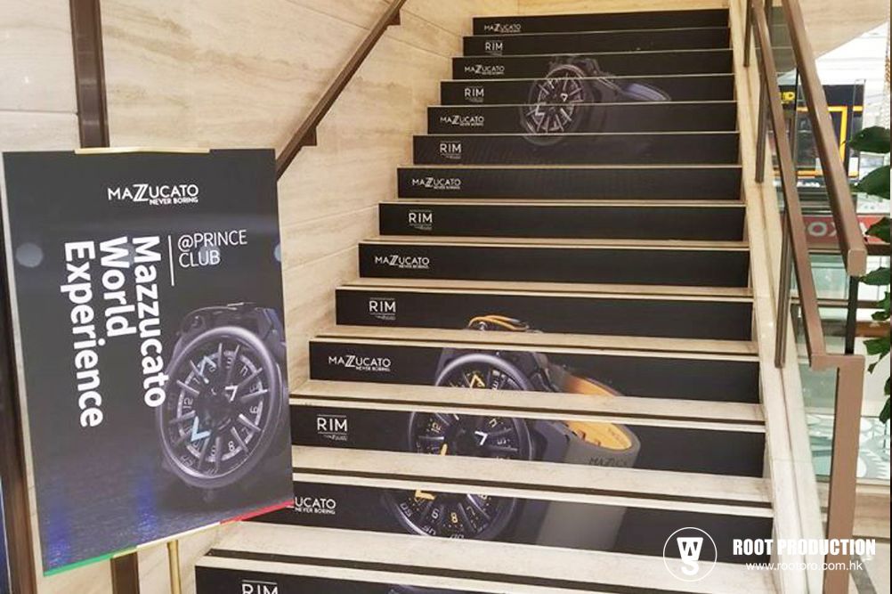 Staircase with Mazzucato World Experience branding; watch image on steps. Sign on left.