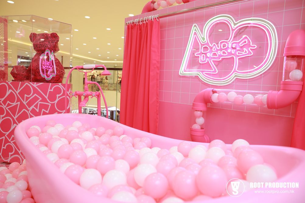 Pink ball pit in a bathtub with pink decor; neon sign in a mall.