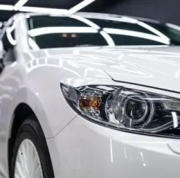 A close-up of the front headlight and bumper of a white Mazda car in a well-lit showroom.
