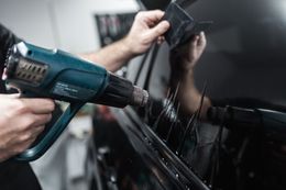 A technician uses a heat gun to apply window tint to a car vehicle.