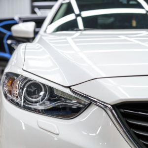 Close-up of the front headlight and grille of a white car parked in a garage with another vehicle in the background.