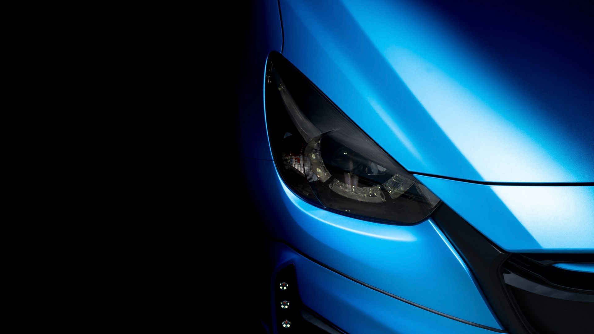 Close-up of a glossy blue car's headlight and hood against a black background.