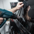 A person uses a heat gun to apply window tint to a car window.