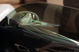 A close-up of a car's tinted driver-side window showing a reflection of the side-view mirror.