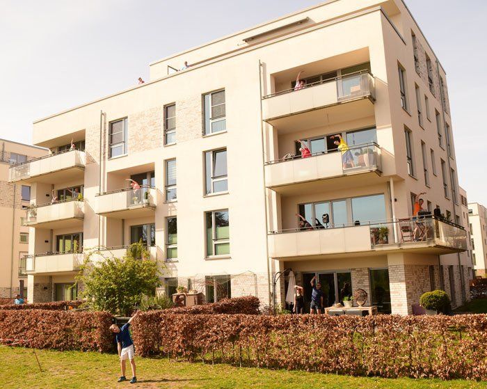 Das Foto zeigt ein Haus in der Nähe des BSVH. Es hat fünf Stockwerke. Auf jedem Balkon stehen Leute in Sportkleidung, die Übungen machen