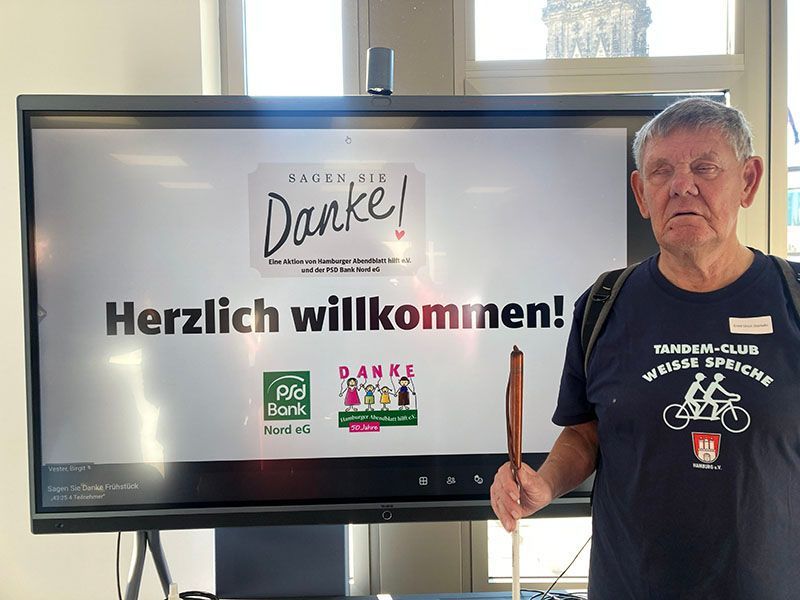 Unser Tourenwart Ulli Staniullo neben dem Bildschirm mit den Logos von Sagen Sie Danke, PSD Bank Nord eG und Hamburger Abendblatt Verein.