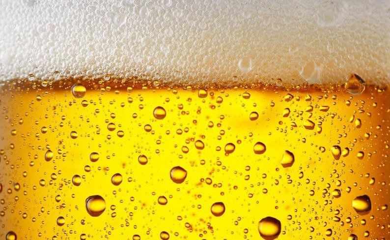 Nahaufnahme von einem Bier: oben schaum, unten das gelbe Bier mit Perlen, die durch die Nahaufnehme ziemlich groß sind.