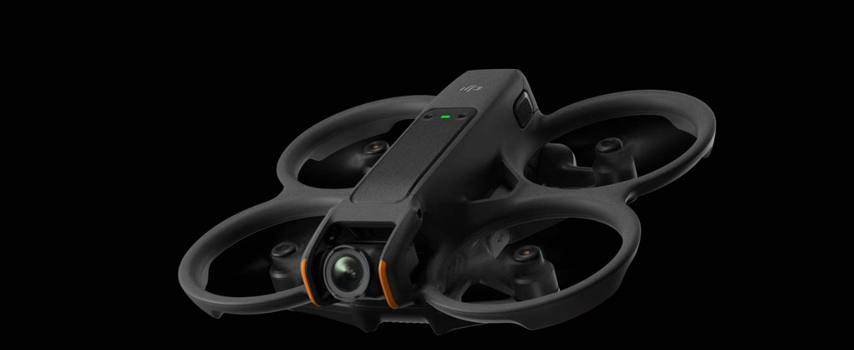 A black drone with a camera attached to it is flying in the air on a black background.