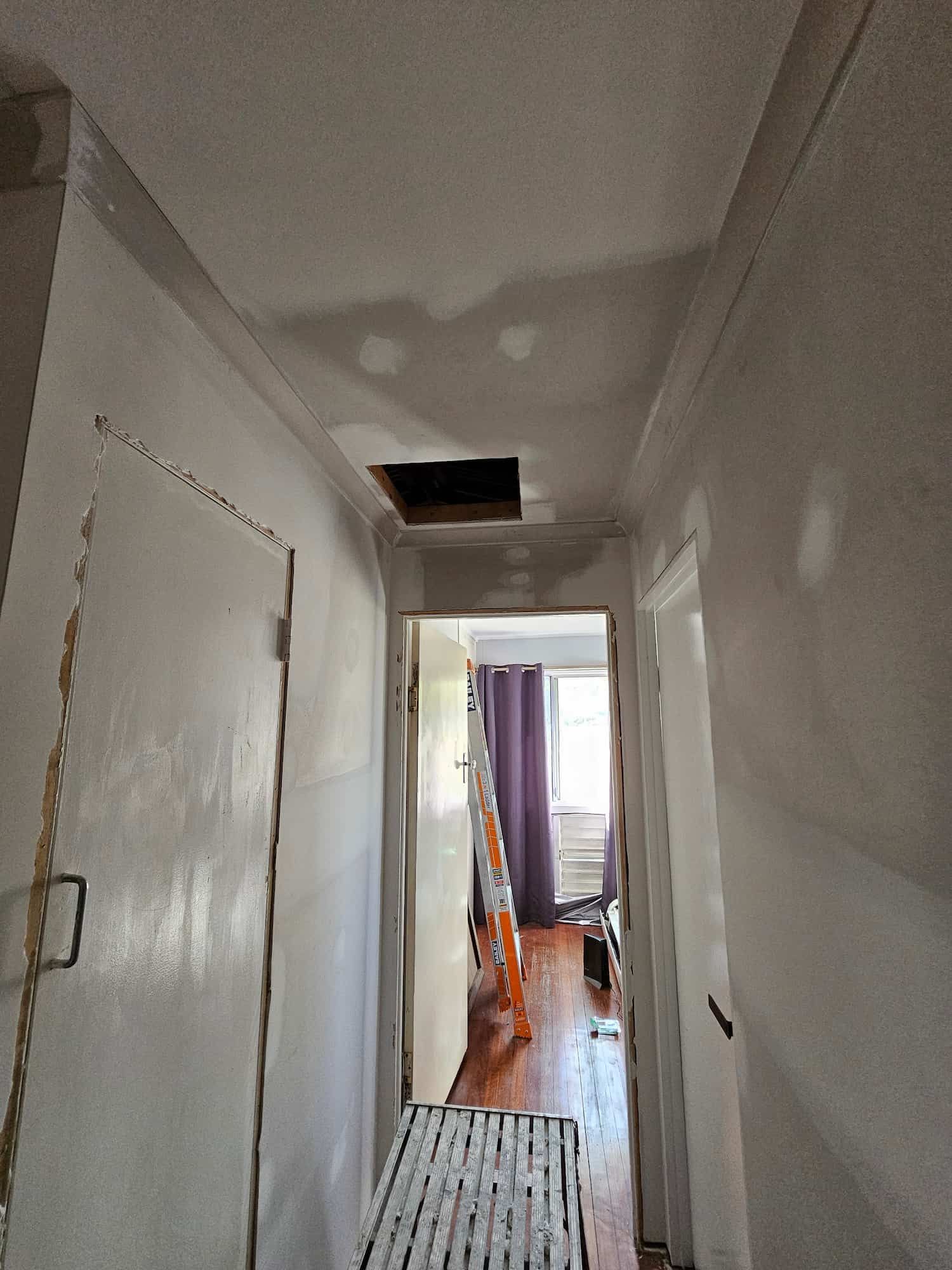 A Hallway With a Hole in the Ceiling and a Ladder — Poljak Plasterers in Annandale, QLD