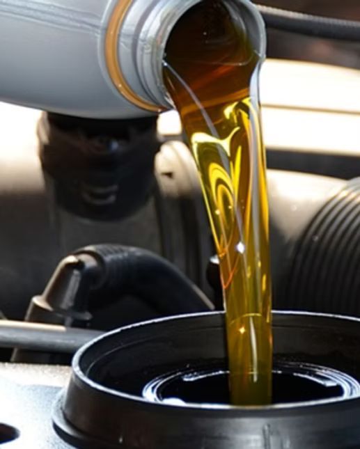 Pouring motor oil into a car engine; yellow-brown liquid from a bottle into a black container.