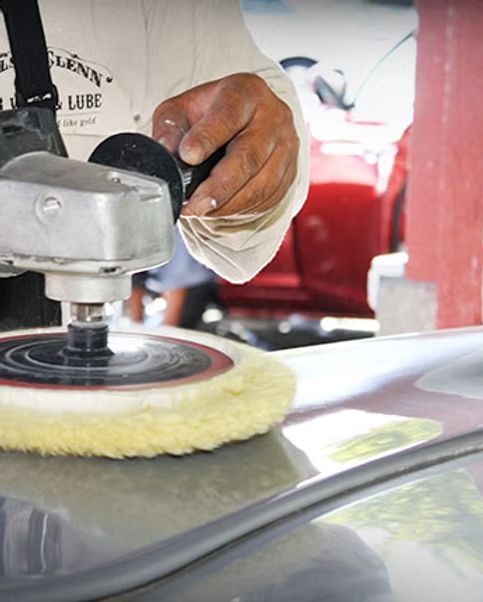 Person polishing a car with a power buffer; hands in gloves, red car in background.