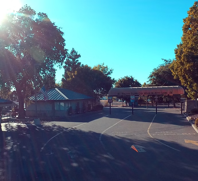 Entrance to Pleasant Hill Swim Club under a bright blue sky, with trees and a building.