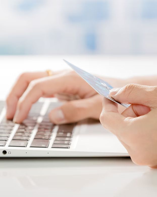 Person typing on a laptop with one hand and holding a credit card in the other.