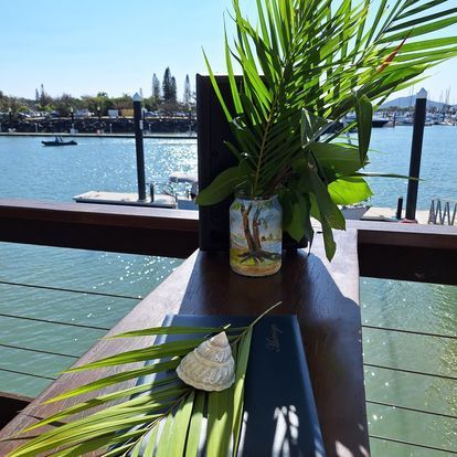 A Table With a Vase of Plants and a Menu on It — ‘Weddings on the Run’ – Elope with the Travelling Celebrant In Emu Park, QLD