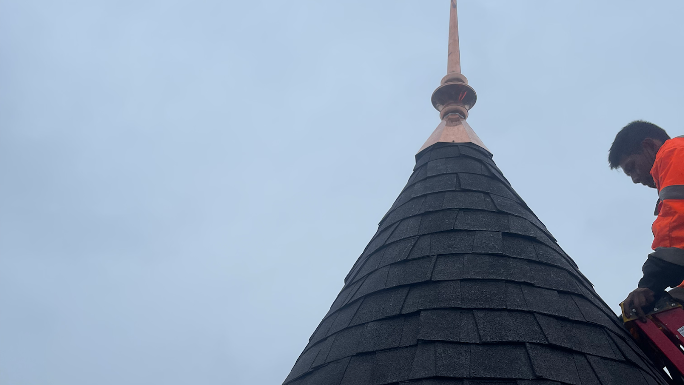 A man is standing on top of a roof with a ladder.