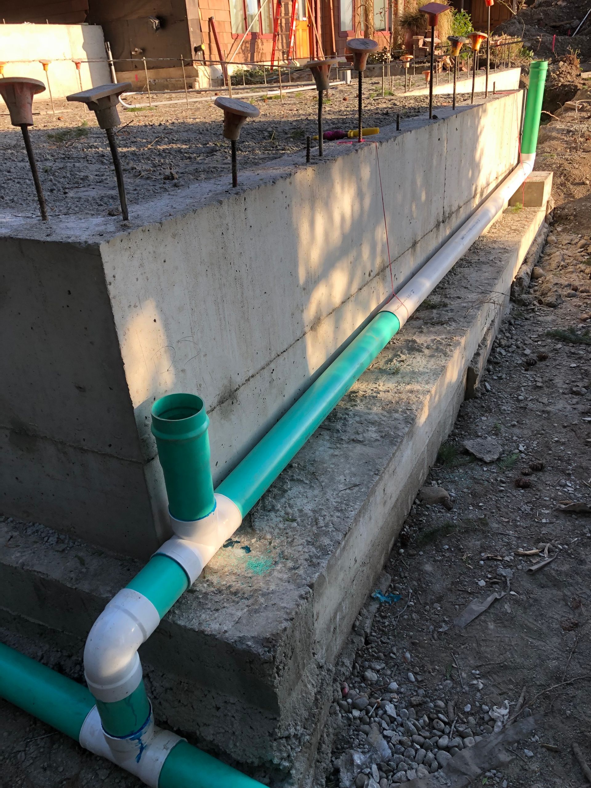 Concrete foundation with green and white PVC pipes attached. Construction site.