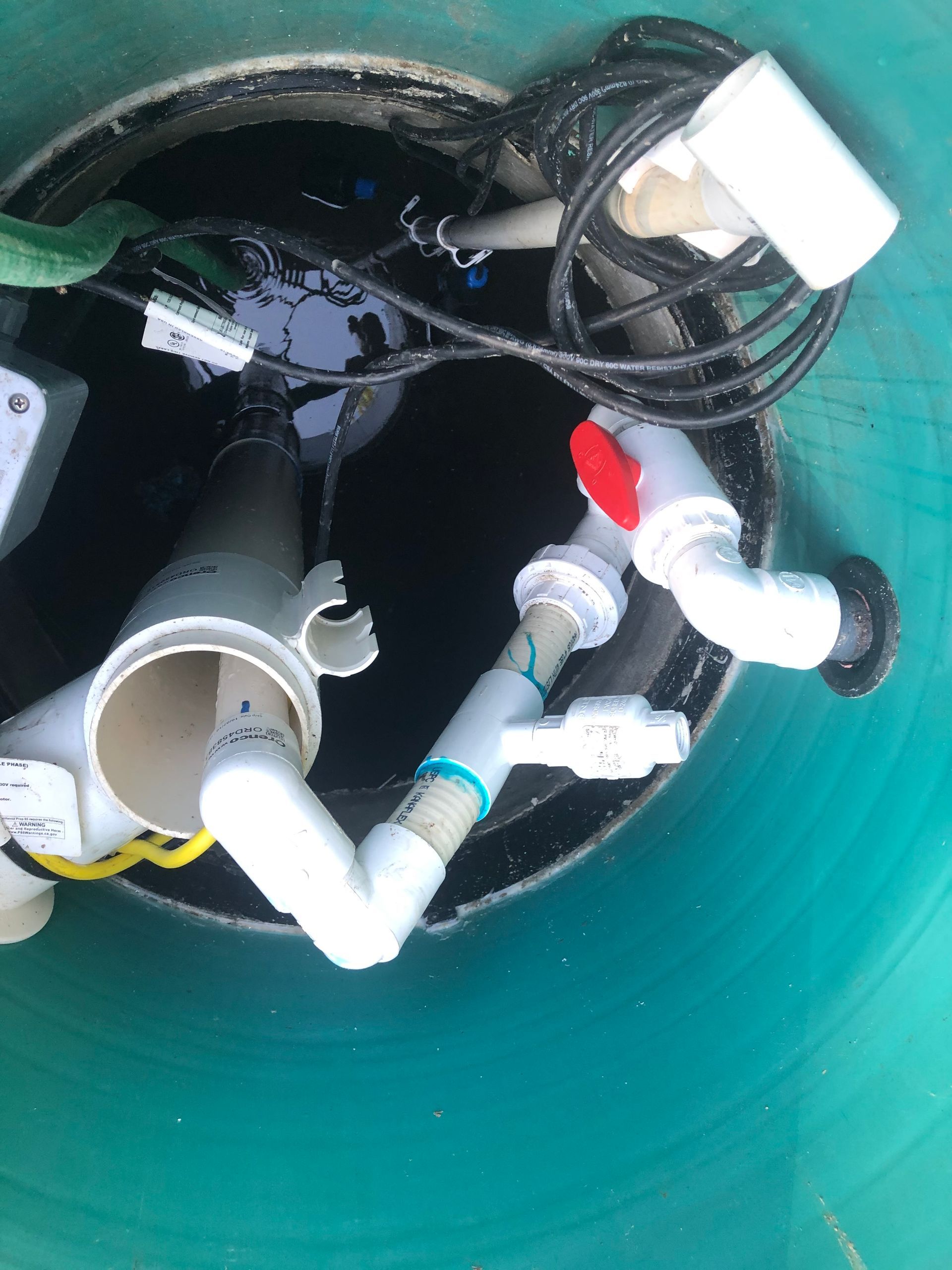 Top-down view of a green water tank with plumbing, electrical wires, and a red valve inside.