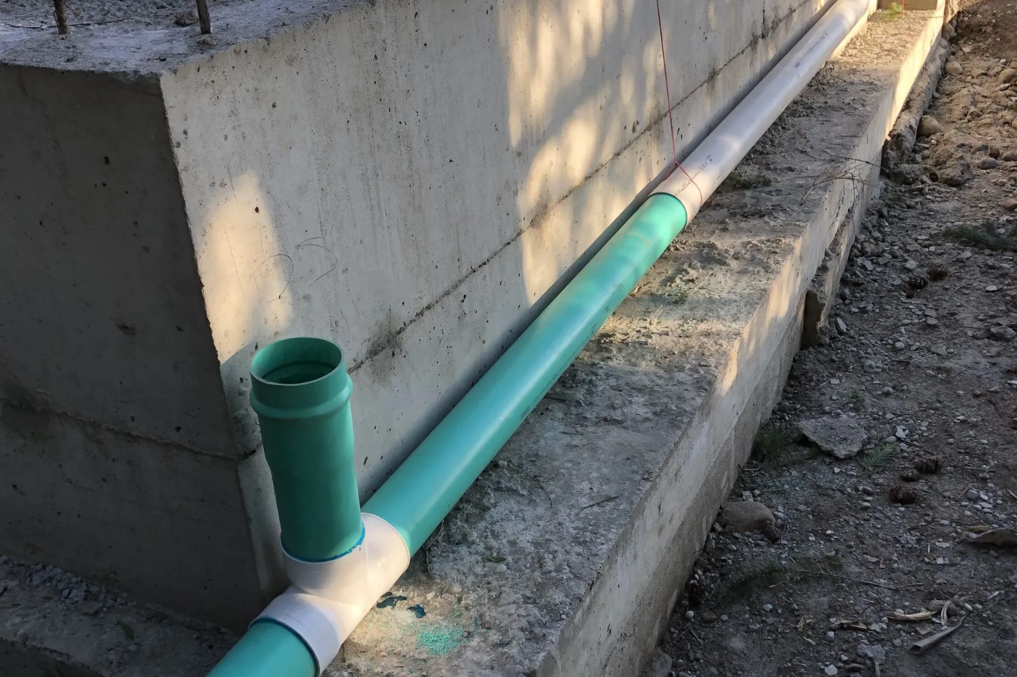 Green and white PVC pipes installed next to a concrete foundation.