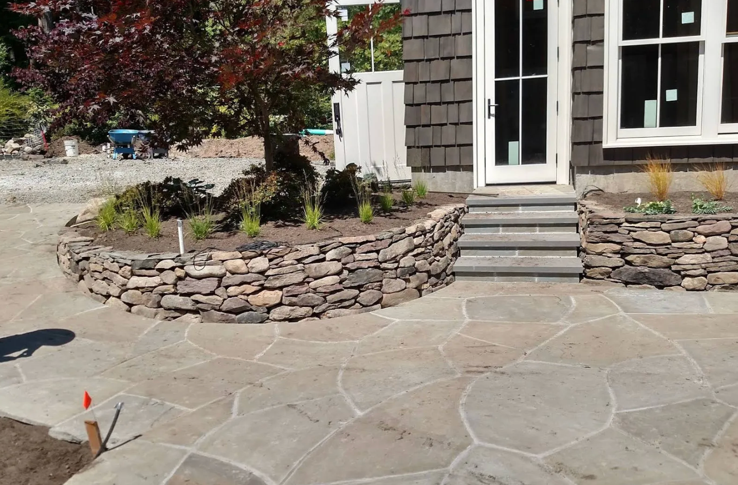 Stone patio with curved stone planter and steps leading to a house entrance.