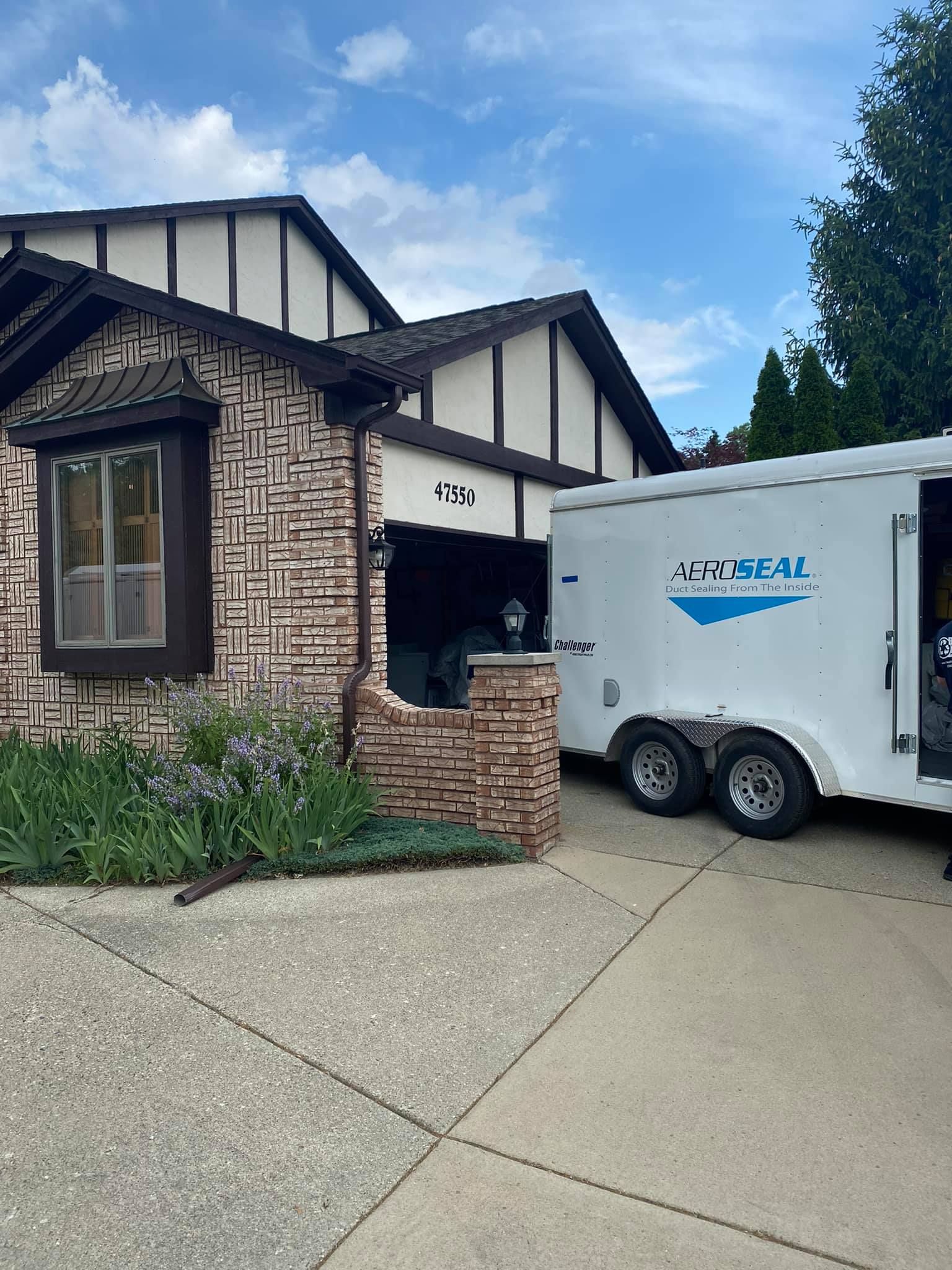 A white trailer is parked in front of a brick house.