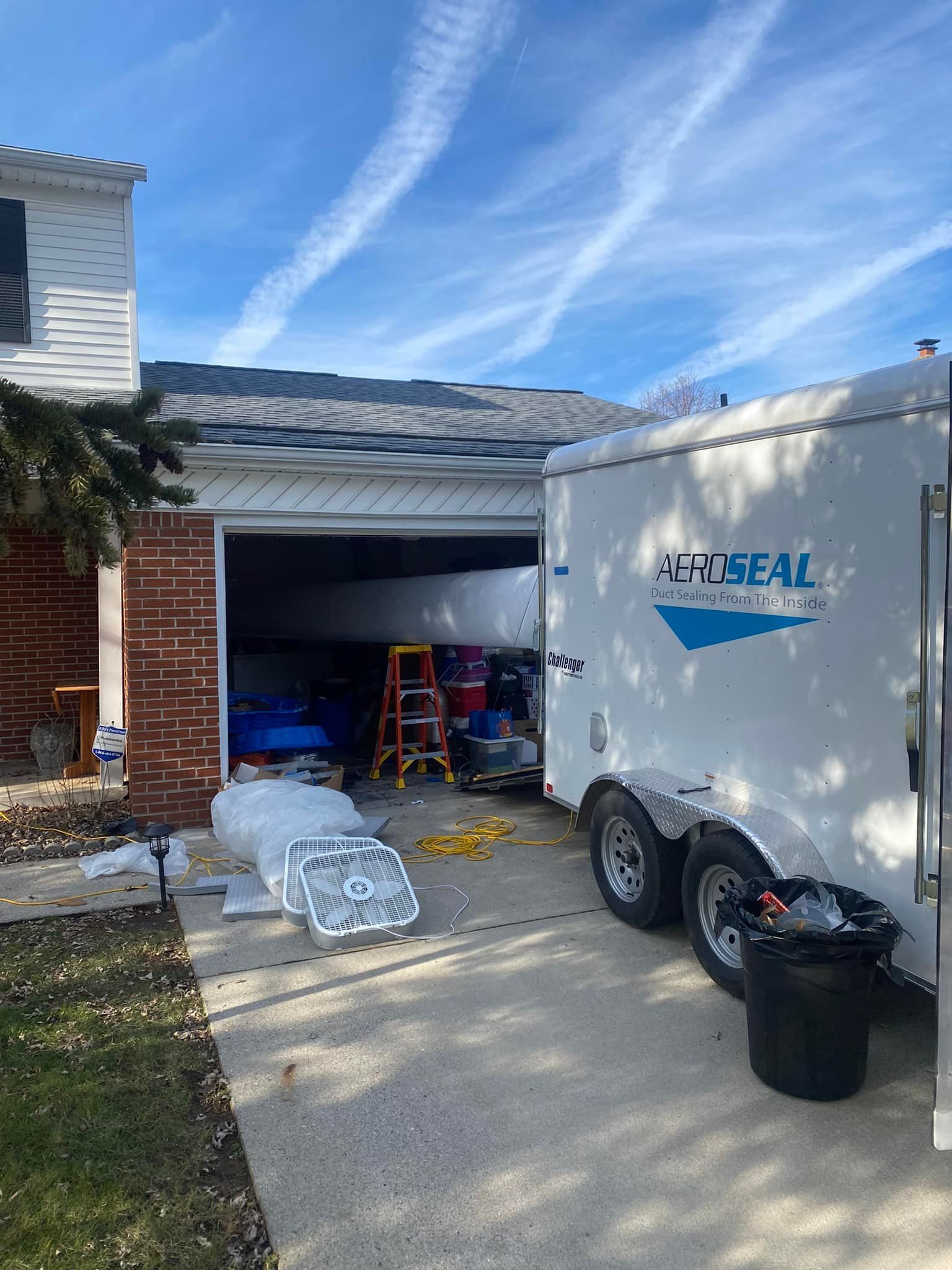A white trailer is parked in front of a garage door.