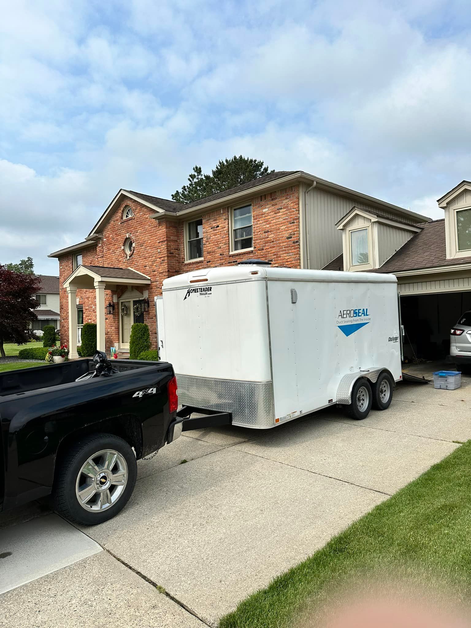 A truck is pulling a white trailer in front of a brick house.