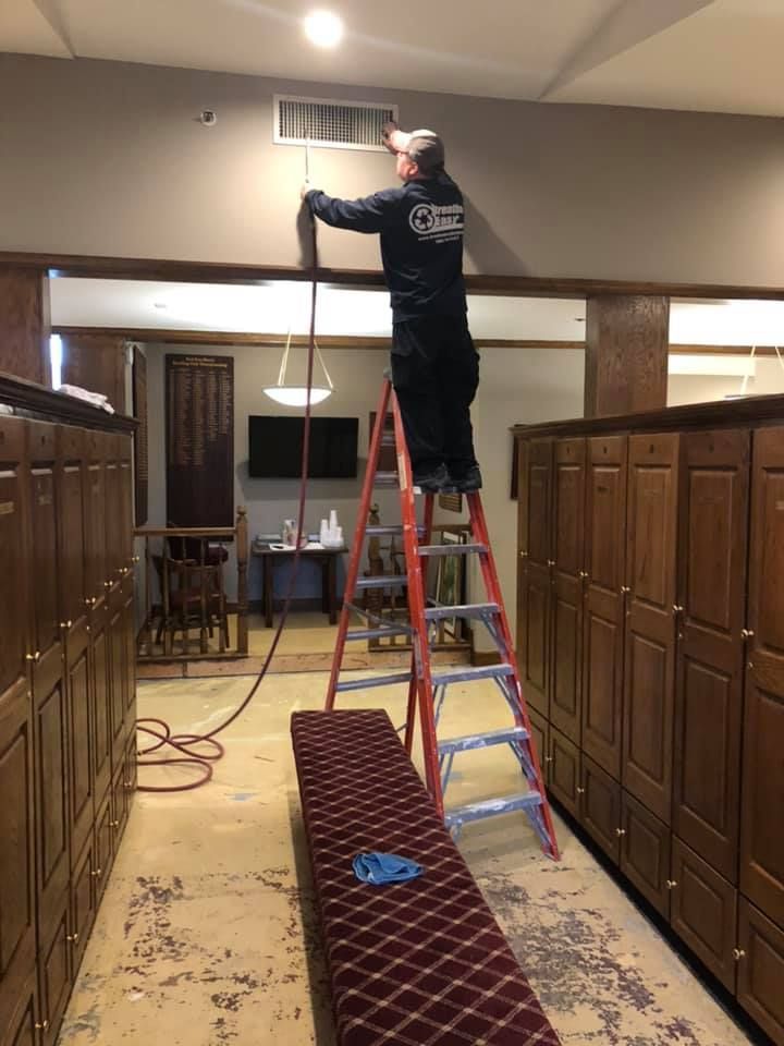 A man is standing on a ladder in a room with lots of cabinets.