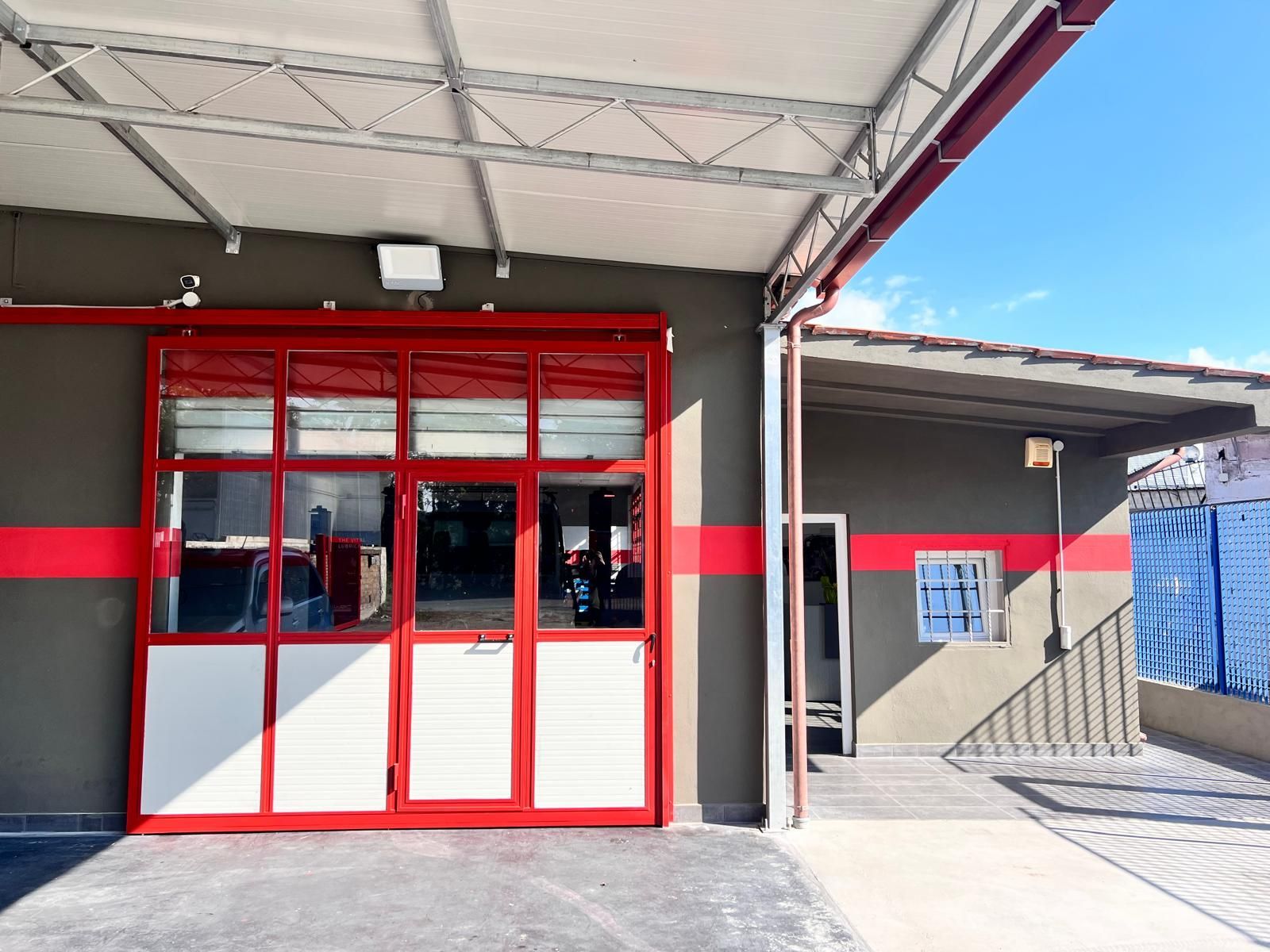 Ingresso del garage con rifiniture rosse, finestre e tettoia, accanto a un piccolo edificio con una porta aperta.