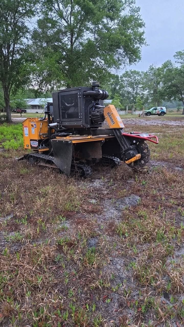 Yellow bulldozer in a muddy field near trees, viewed from behind.