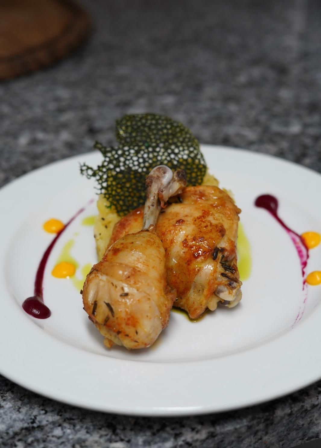 Piatto di cosce di pollo cotte su purè di patate, guarnite con caviale e salse colorate.