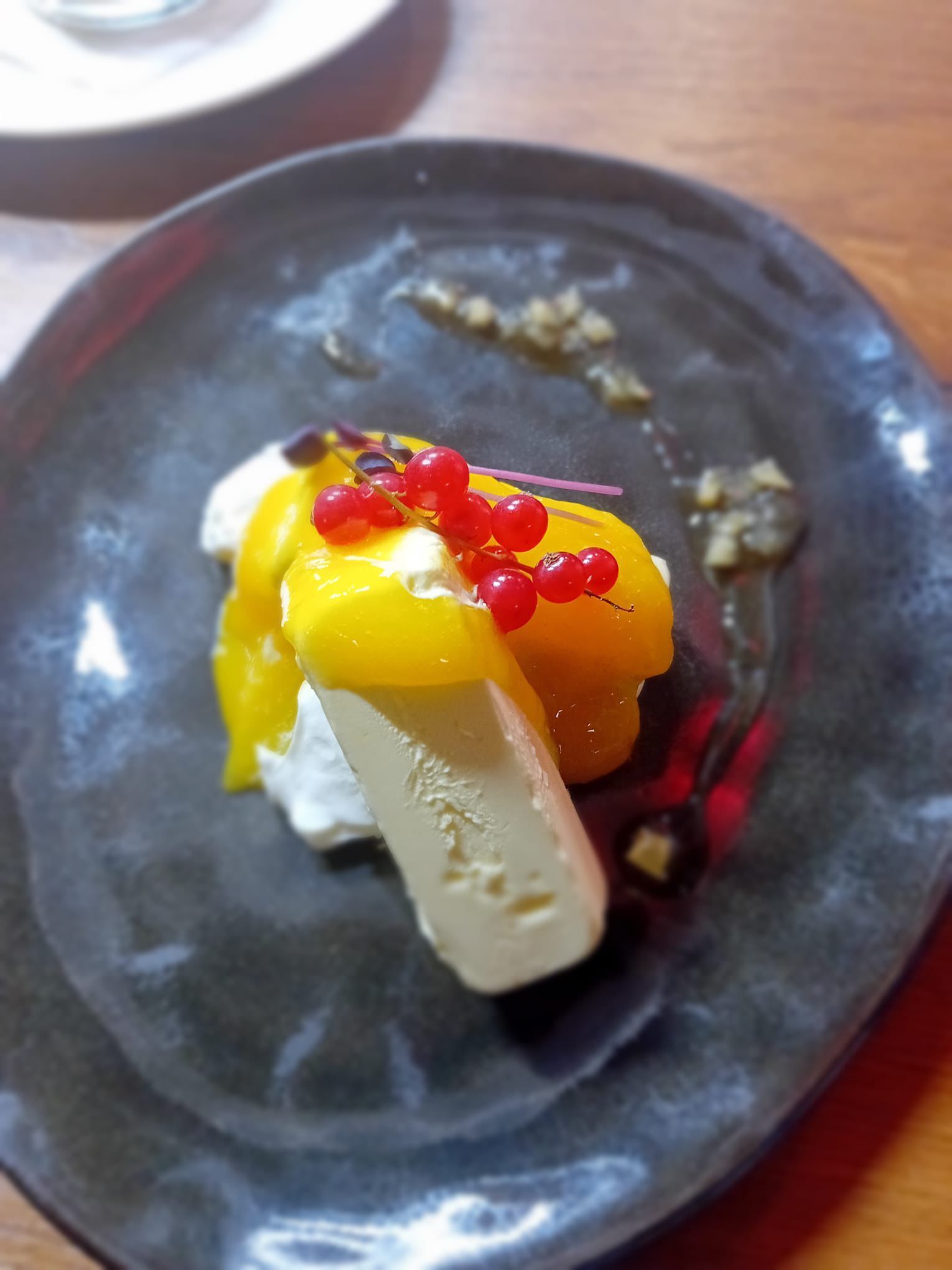 Dessert su un piatto scuro: gelato con frutta gialla, bacche rosse e un filo di salsa.