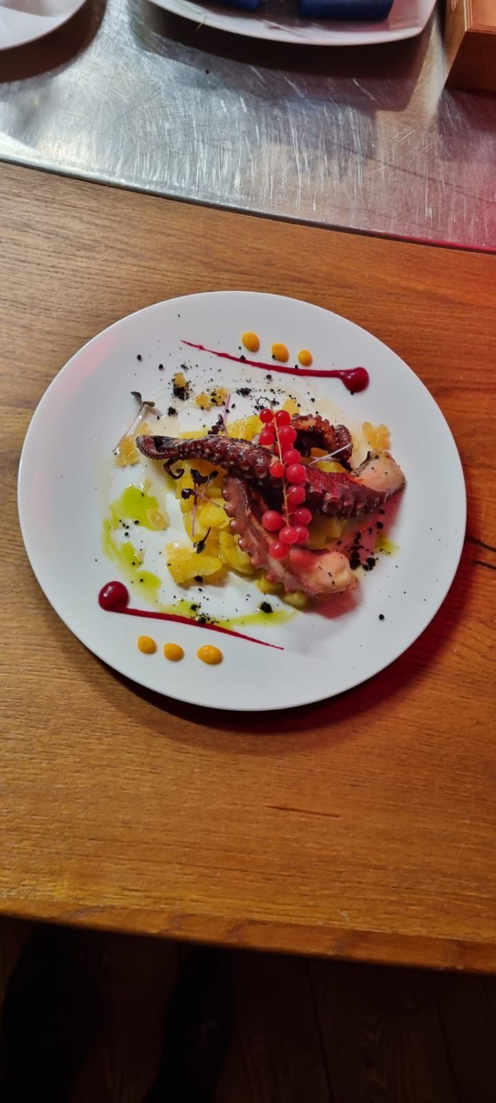 Piatto di cibo con polpo, frutti di bosco e salsa su un tavolo di legno.
