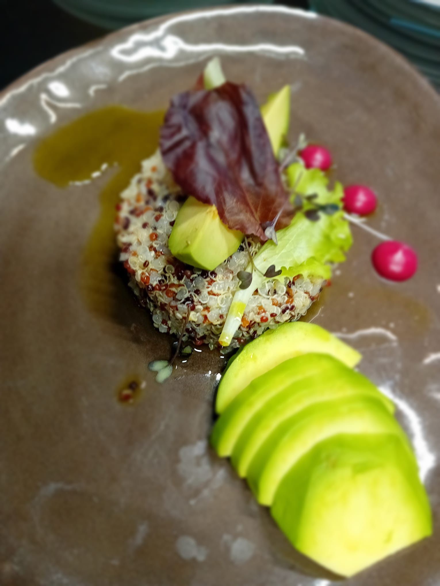 Insalata di quinoa con fette di avocado, verdure e ravanelli su un piatto marrone.