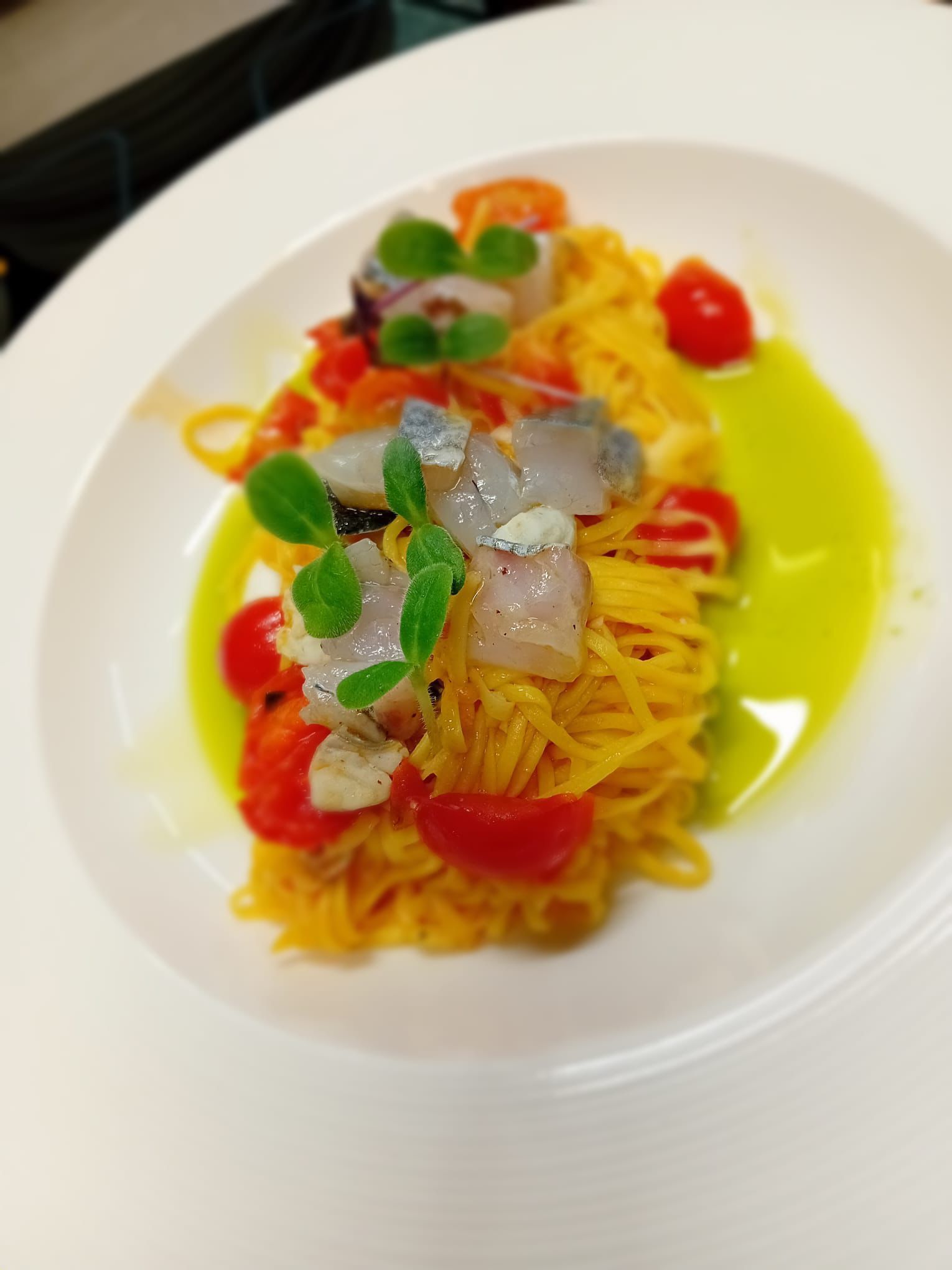 Piatto di pasta con pomodori, pesce e salsa verde, presentato su un piatto bianco.